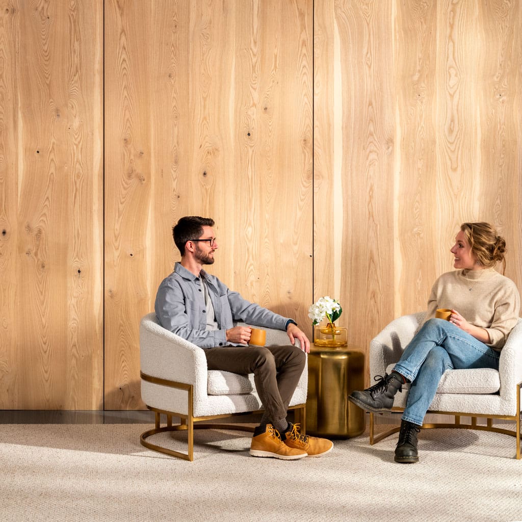 Two people sit in chairs in a living room with Select Heart Ash Veneer Wood Wall Paneling