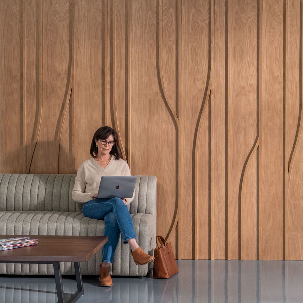 Woman working in front of White Oak Tributary Dimensional Wood Wall Paneling in a modern office setting