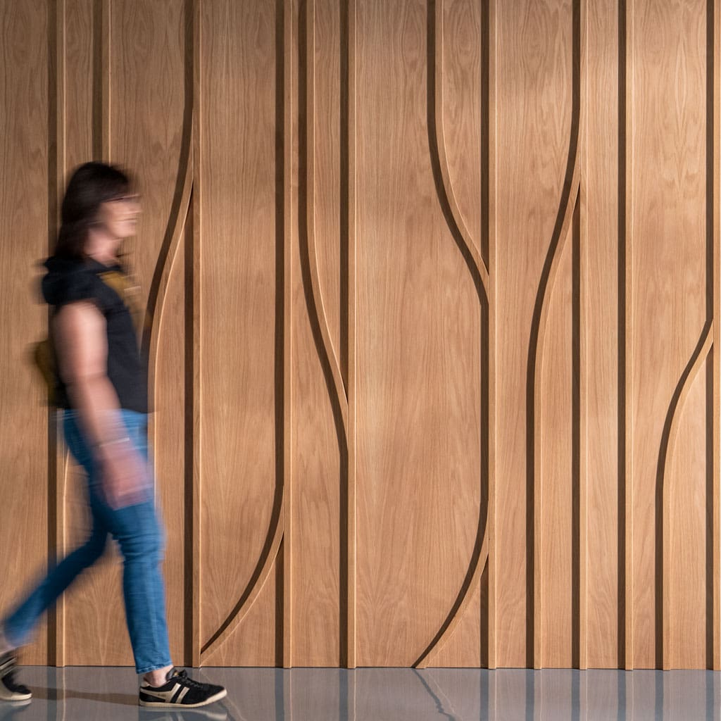 Woman walking in front of white oak dimensional wood wall paneling